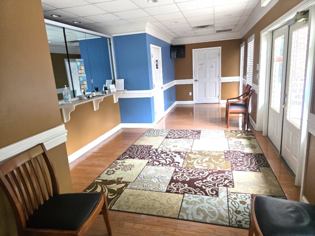 Bright dental office lobby with blue and tan walls, featuring a patterned area rug and wooden chairs