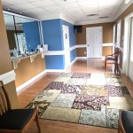 Bright dental office lobby with blue and tan walls, featuring a patterned area rug and wooden chairs