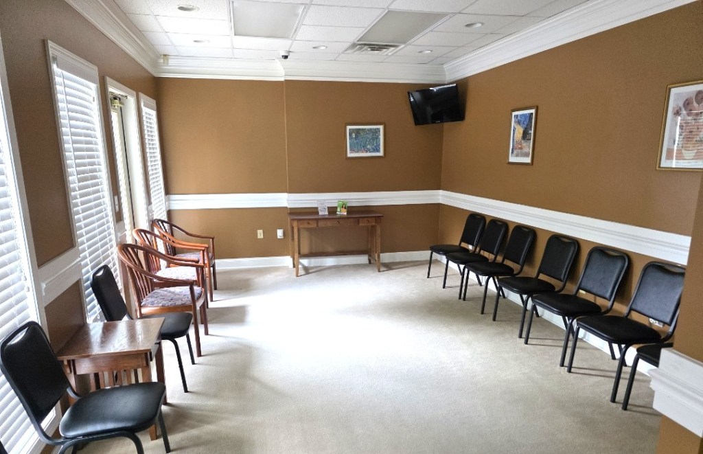 Spacious waiting room with neutral carpeting and rows of black chairs along the walls